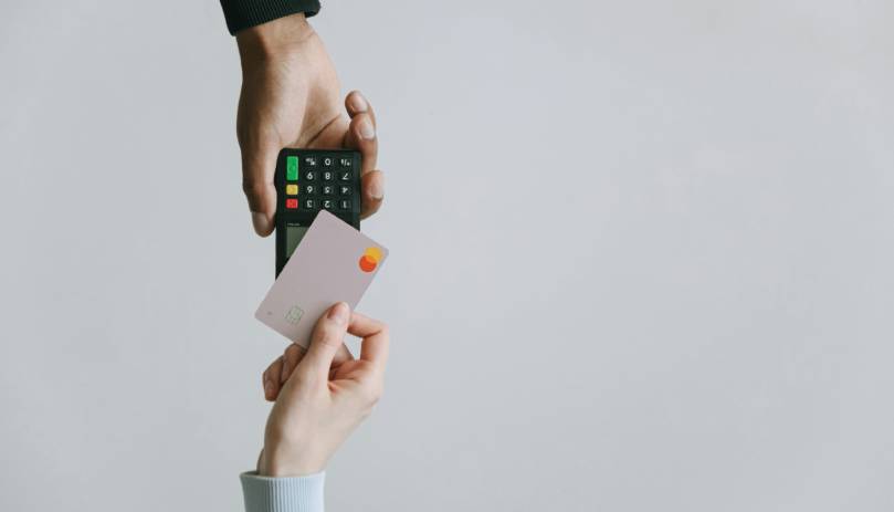 A person holds a credit card in one hand and a remote control in the other, suggesting a shopping or entertainment context.