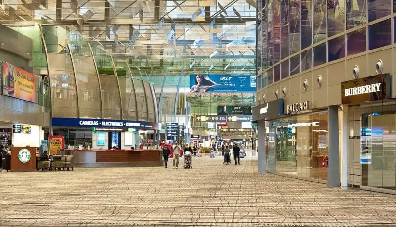 Inside a modern airport terminal with shops, large windows, and travelers walking.