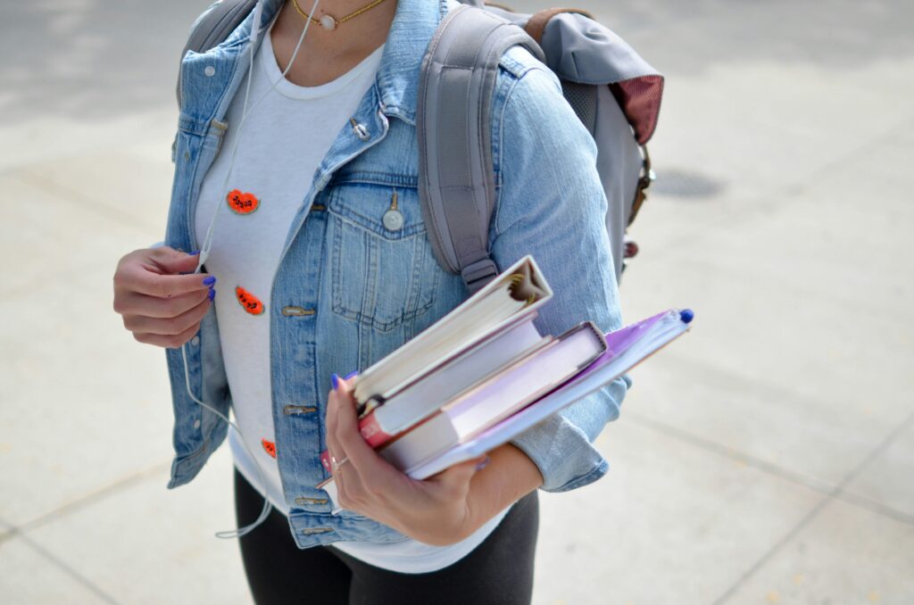 student wearing denim jacket with white tshirt and backpack carrying books